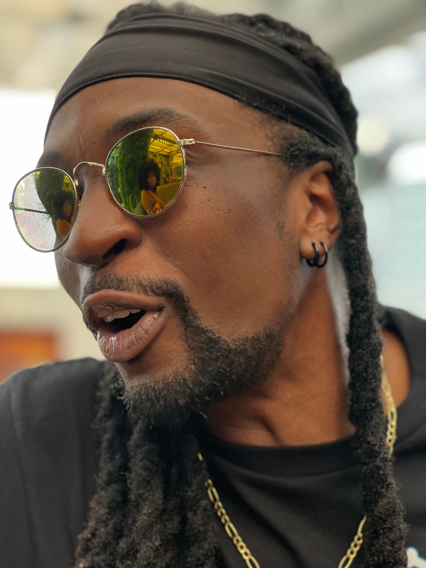 Close-up of a man wearing reflective aviator sunglasses and a black headband with braided hair.